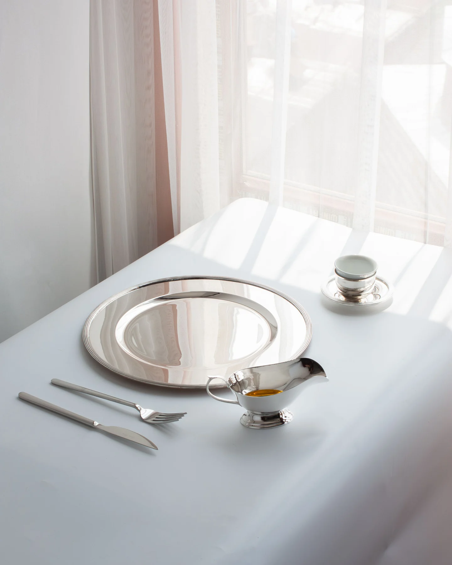Besteck und Porzellanbecher im Licht eines Fensters